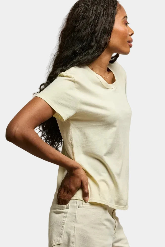 Woman wearing a white t-shirt and light-colored pants against a neutral background