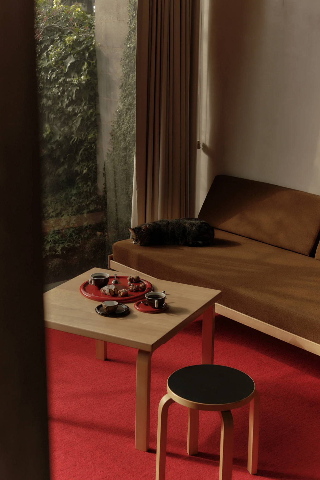 Small table with cups and saucers next to a brown sofa in a room with red carpet.