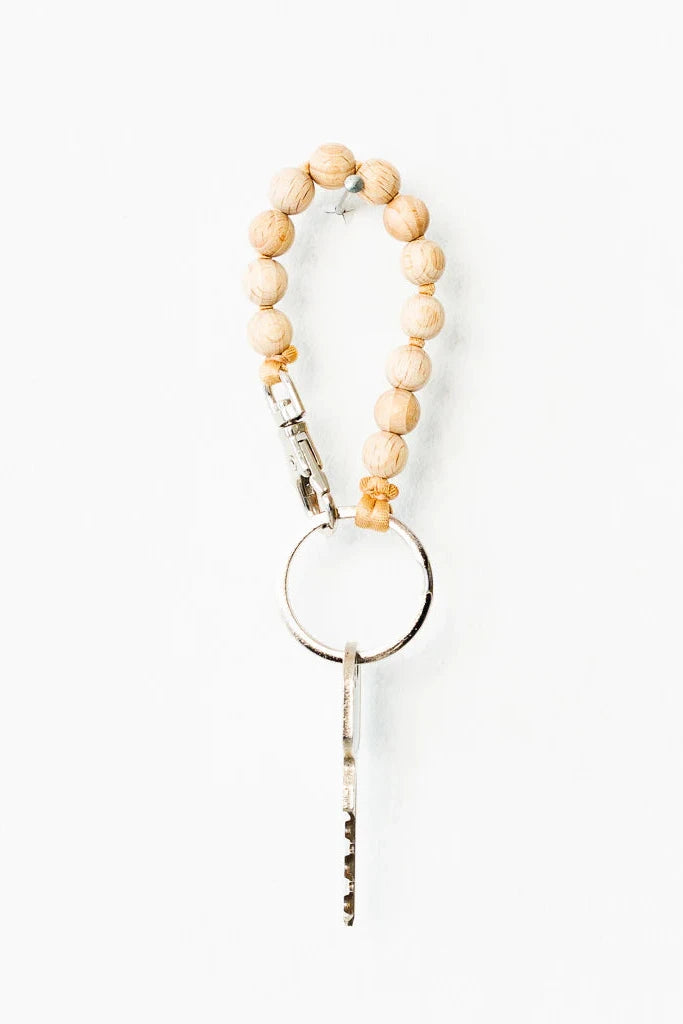 A beige and natural color keychain with a metal ring and a small bell, featuring a series of wooden beads.