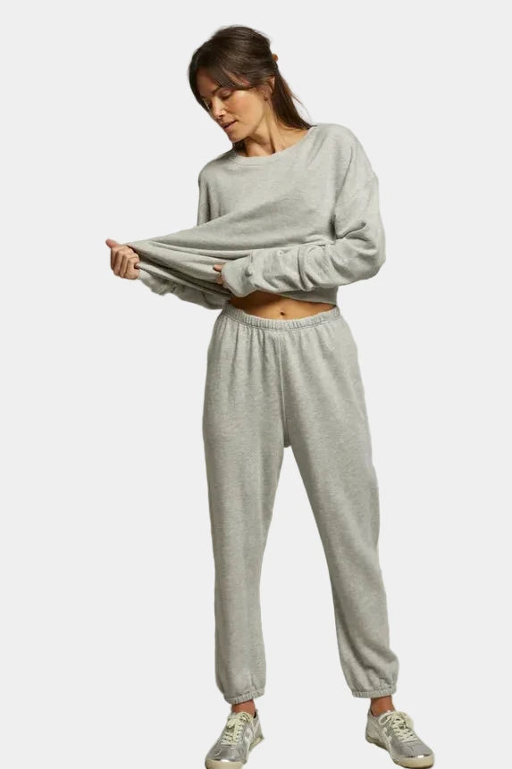 Woman wearing a gray sweatshirt and pants set against a plain background