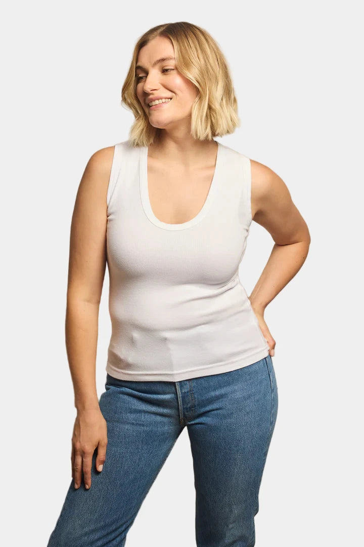 Woman wearing a white tank top and blue jeans against a grey background