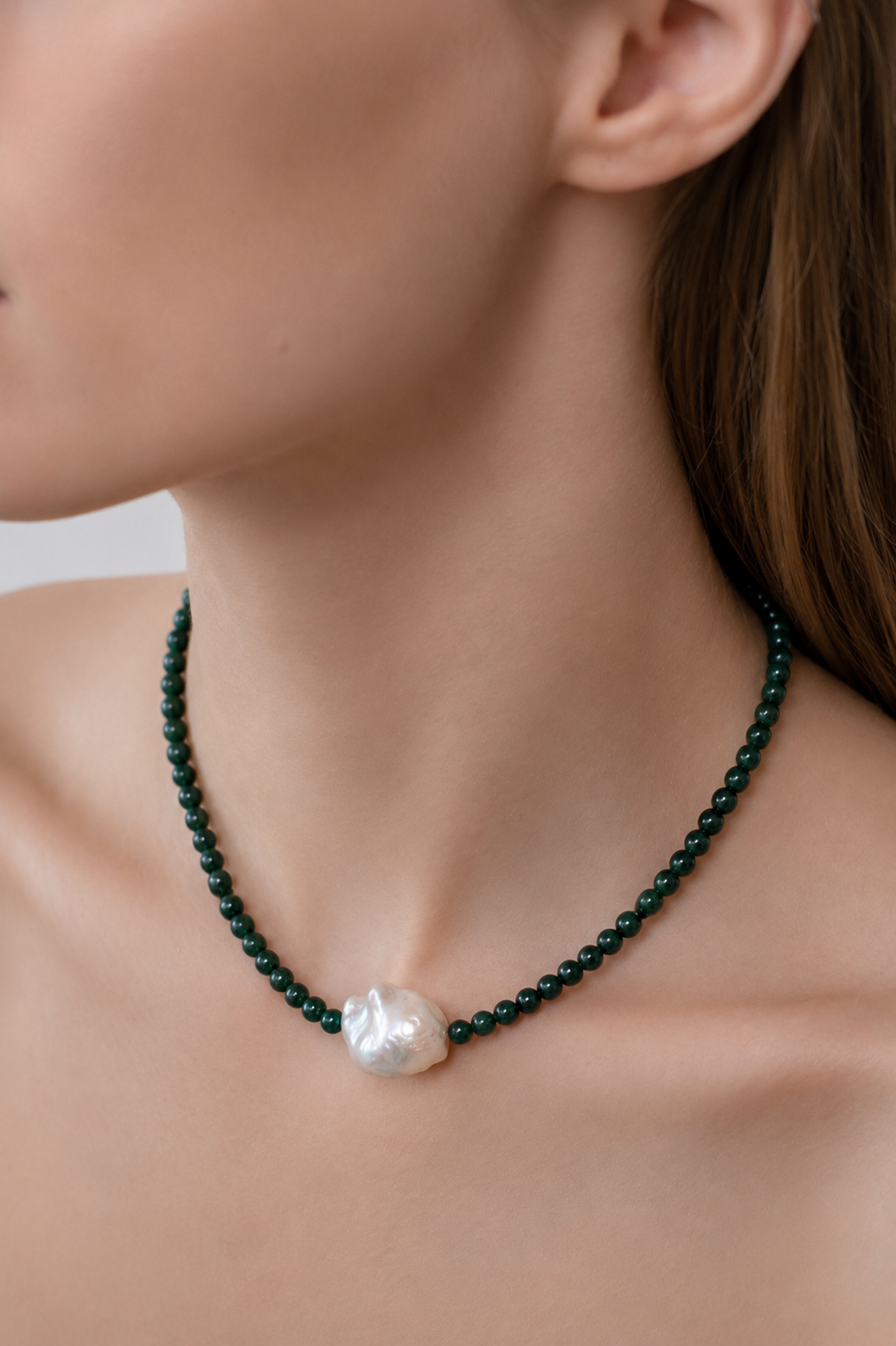 Green beaded necklace with a central baroque pearl on a person's neck