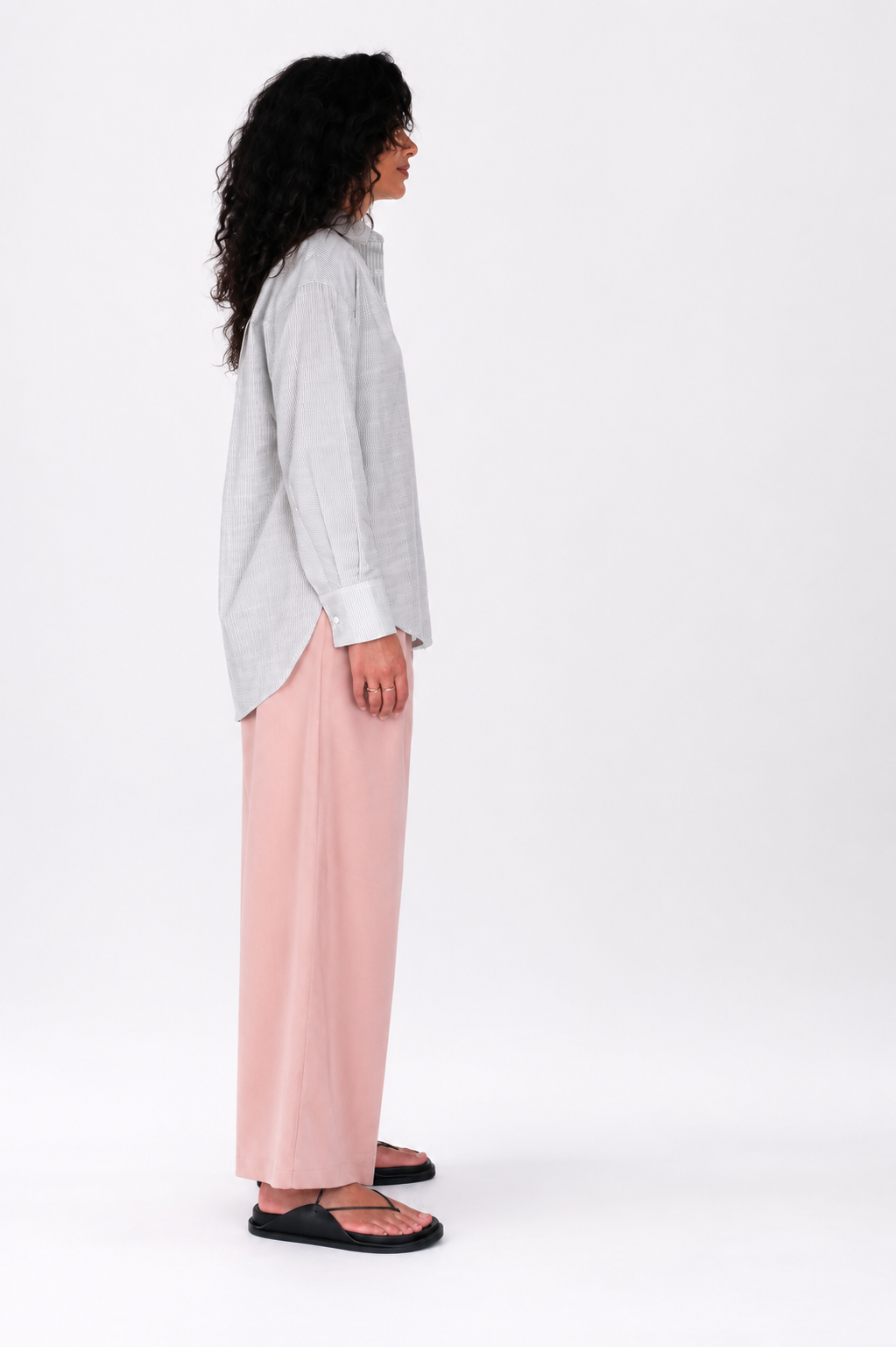 Person wearing a light gray button-up shirt and pink pants on a white background