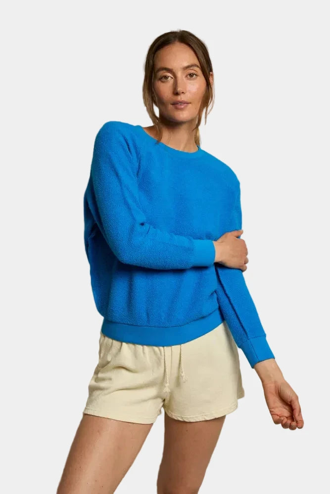 Woman wearing a blue sweater and beige shorts against a neutral background