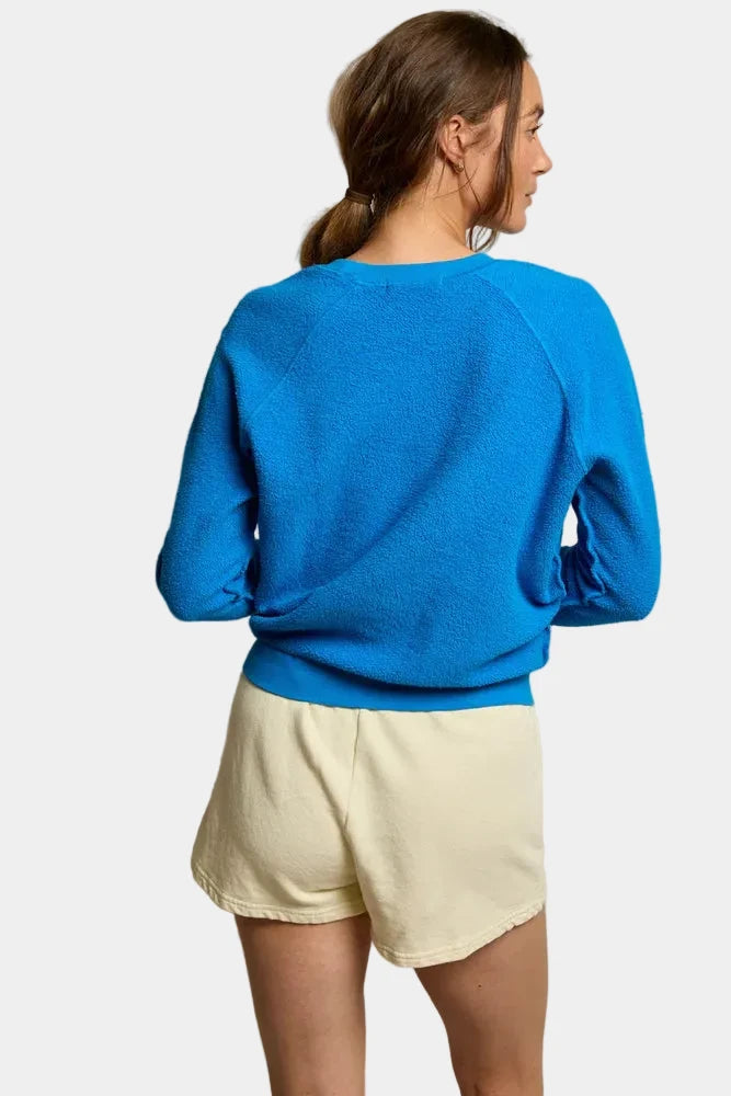 Person wearing a blue sweater and light yellow shorts against a plain background