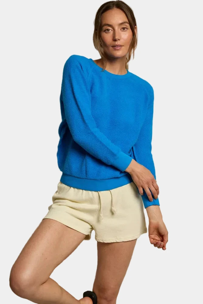 Woman wearing a blue sweater and beige shorts against a neutral background