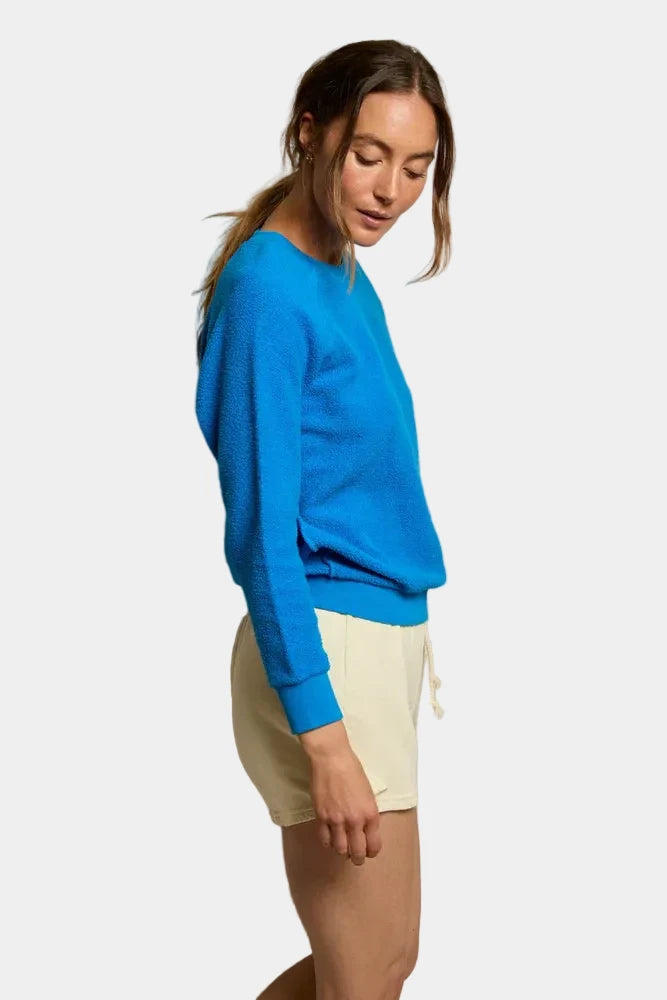 Woman wearing a blue sweater and white shorts against a plain background