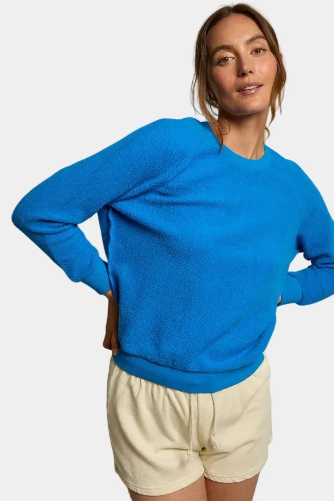 Woman wearing a blue sweater and beige shorts against a plain background