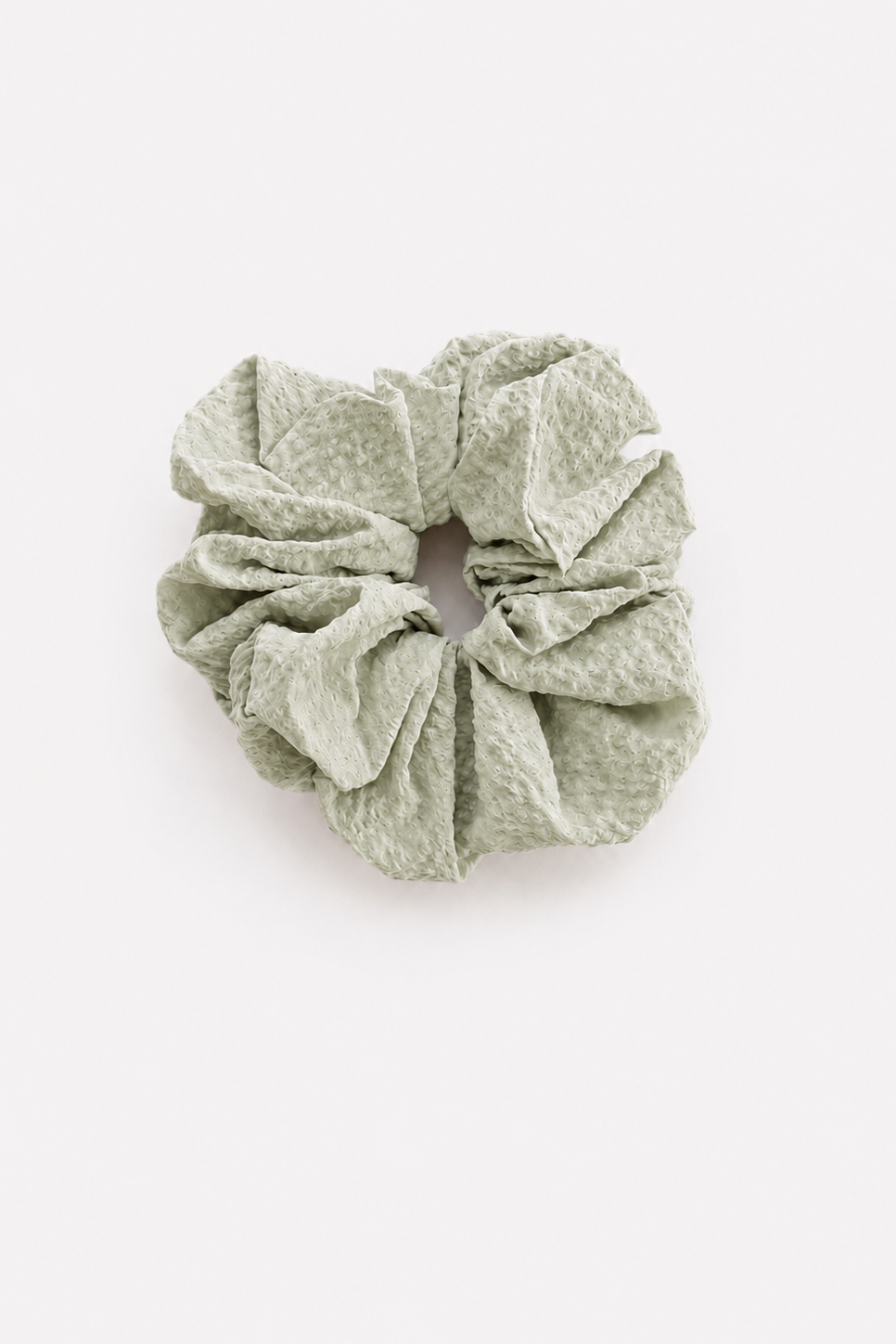 A single crinkled fabric scrunchie in a muted sage green color, photographed from directly above on a clean white background - East Coast General