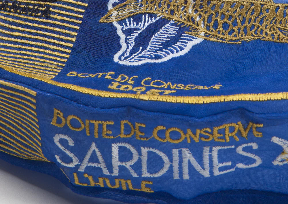 Close-up of a blue and gold canister with embroidered text on a white background