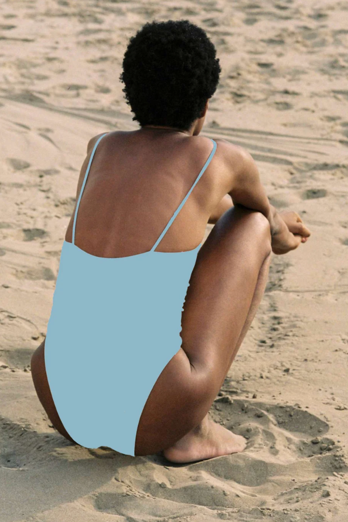Person sitting on a sandy beach wearing a light blue swimsuit.